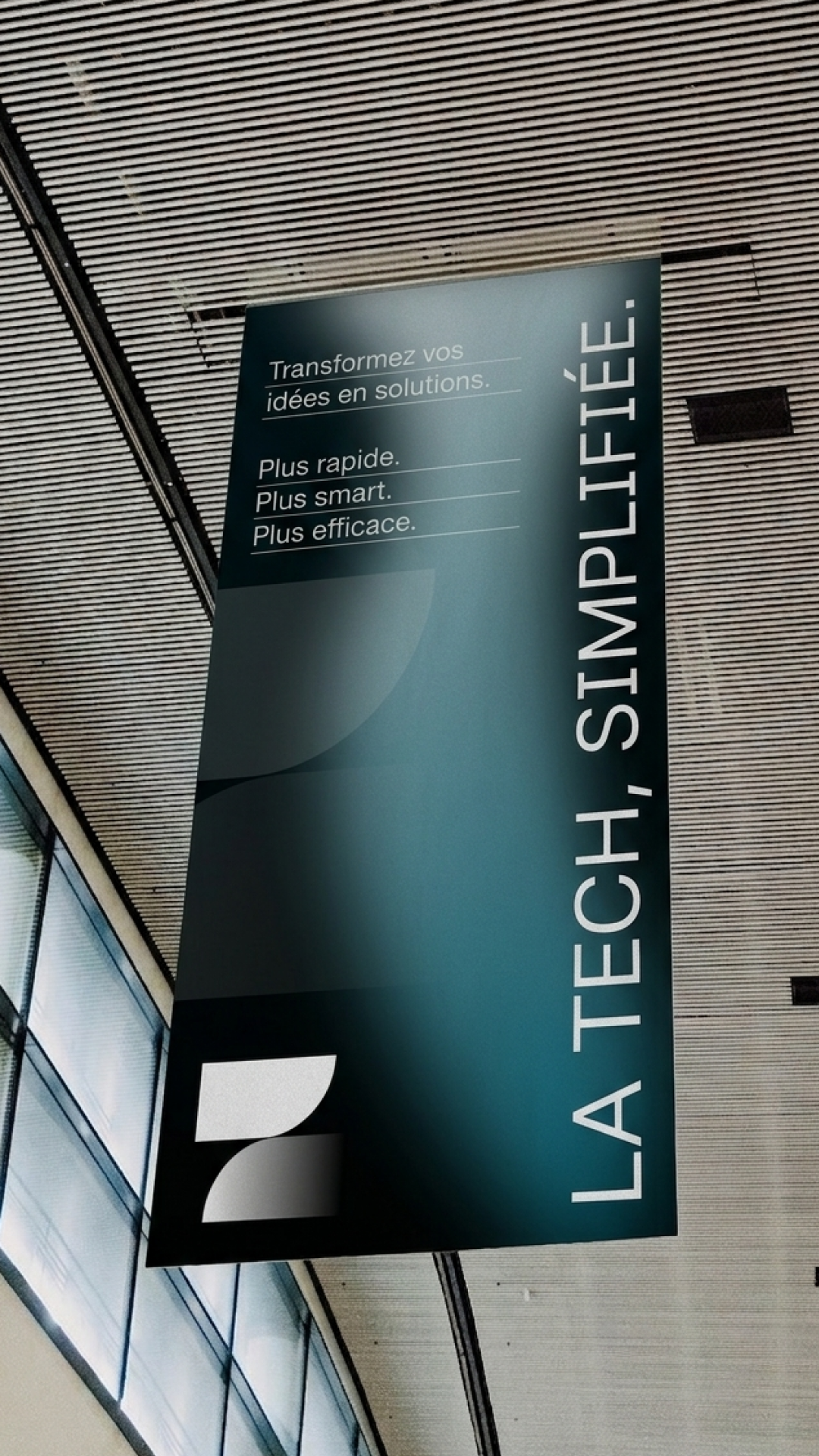 Une bannière publicitaire dans un hall moderne avec un plafond en lames de bois, encourageant à transformer les idées en solutions plus rapidement, plus intelligemment et plus efficacement.