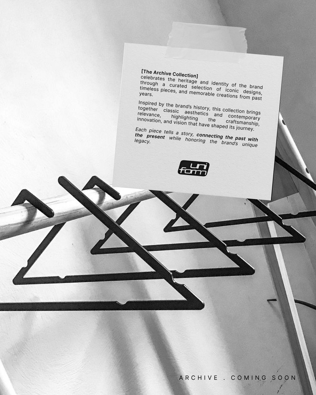 Une affiche blanche avec du texte en anglais sur un fond en noir et blanc, posée sur un support à vêtements vide. En bas à droite, la phrase "ARCHIVE. COMING SOON" est visible.
