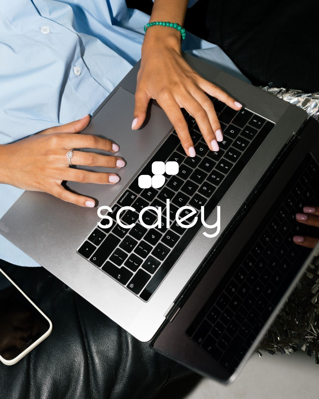 Deux personnes utilisent un ordinateur portable, une personne avec une bague et bracelet vert, une autre avec un close-up de main et une chemise bleue, sur une surface sombre.