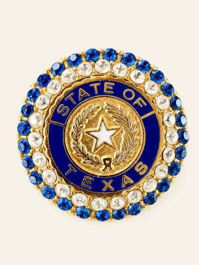 A decorative pin and pendant featuring the Texas state seal surrounded by blue and clear rhinestones.