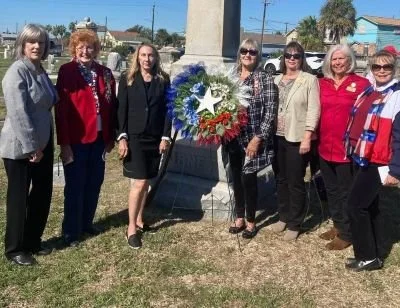 Group of seven women standing outdoors around the Burnet Sherman Monument with a wreath