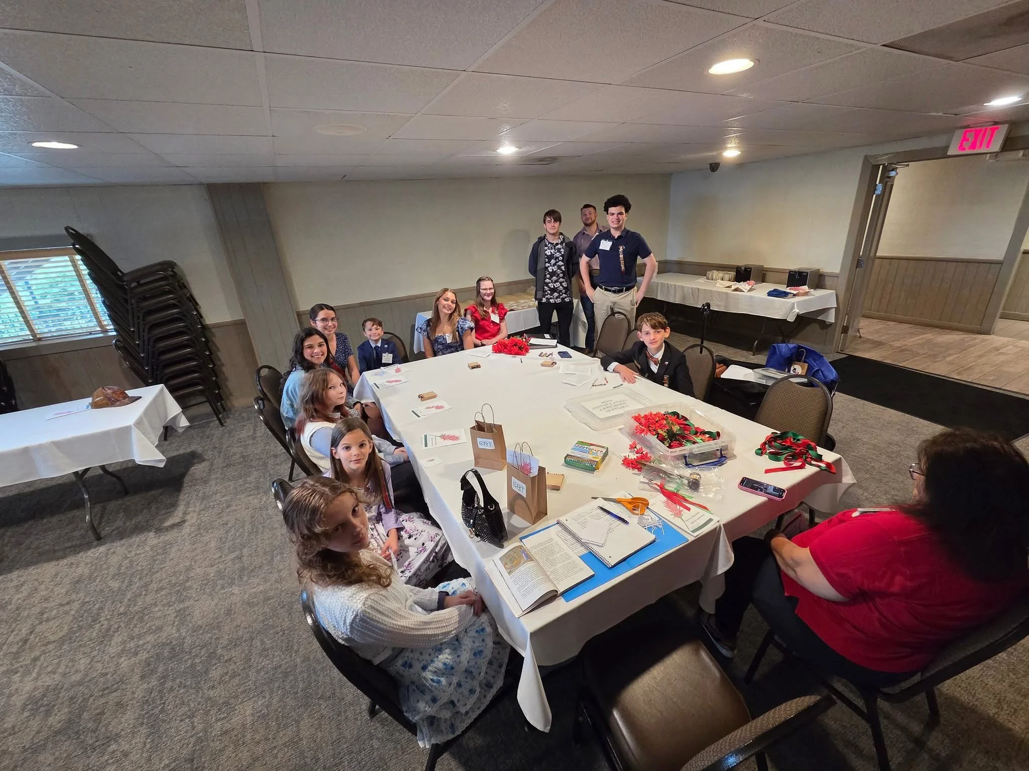 CRT children and teenagers sitting and standing around a large round table working on a project