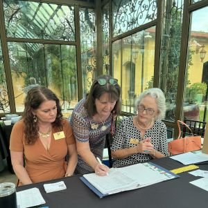 DRT members sitting at a table at the Conservatory of the Bryan Museum at the DRT Workshop with one woman writing or signing a document while the other two observe.