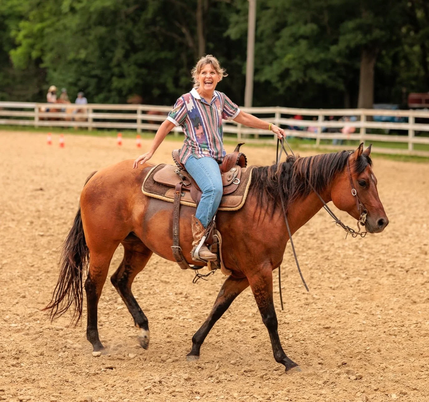 Women riding a brown horse in an outdoor arena, smiling and enjoying the ride.