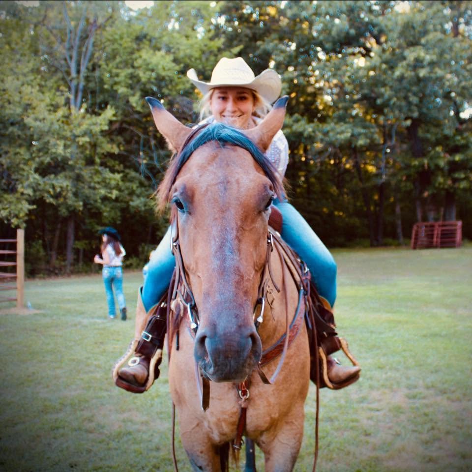 A girl wearing a cowboy hat riding a brown horse outdoors in a grassy area with trees in the background.