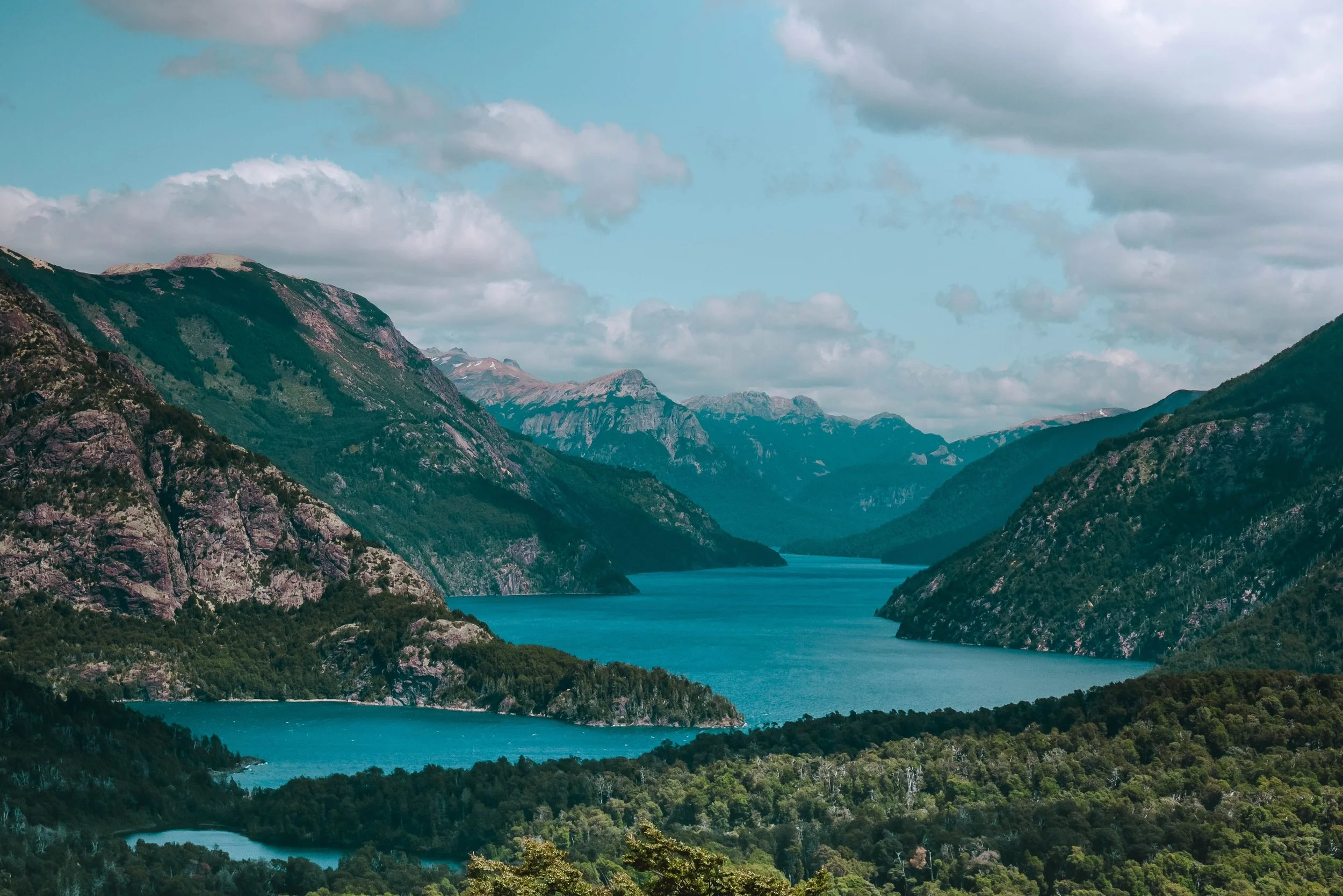 A long turquoise lake winding between forested mountains and rocky peaks in Argentina's Lake District.