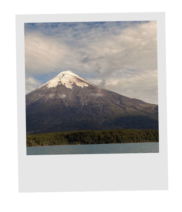 The snowcapped cone of Osorno Volcano rising above a forested lakeshore in Chile's Lake District.