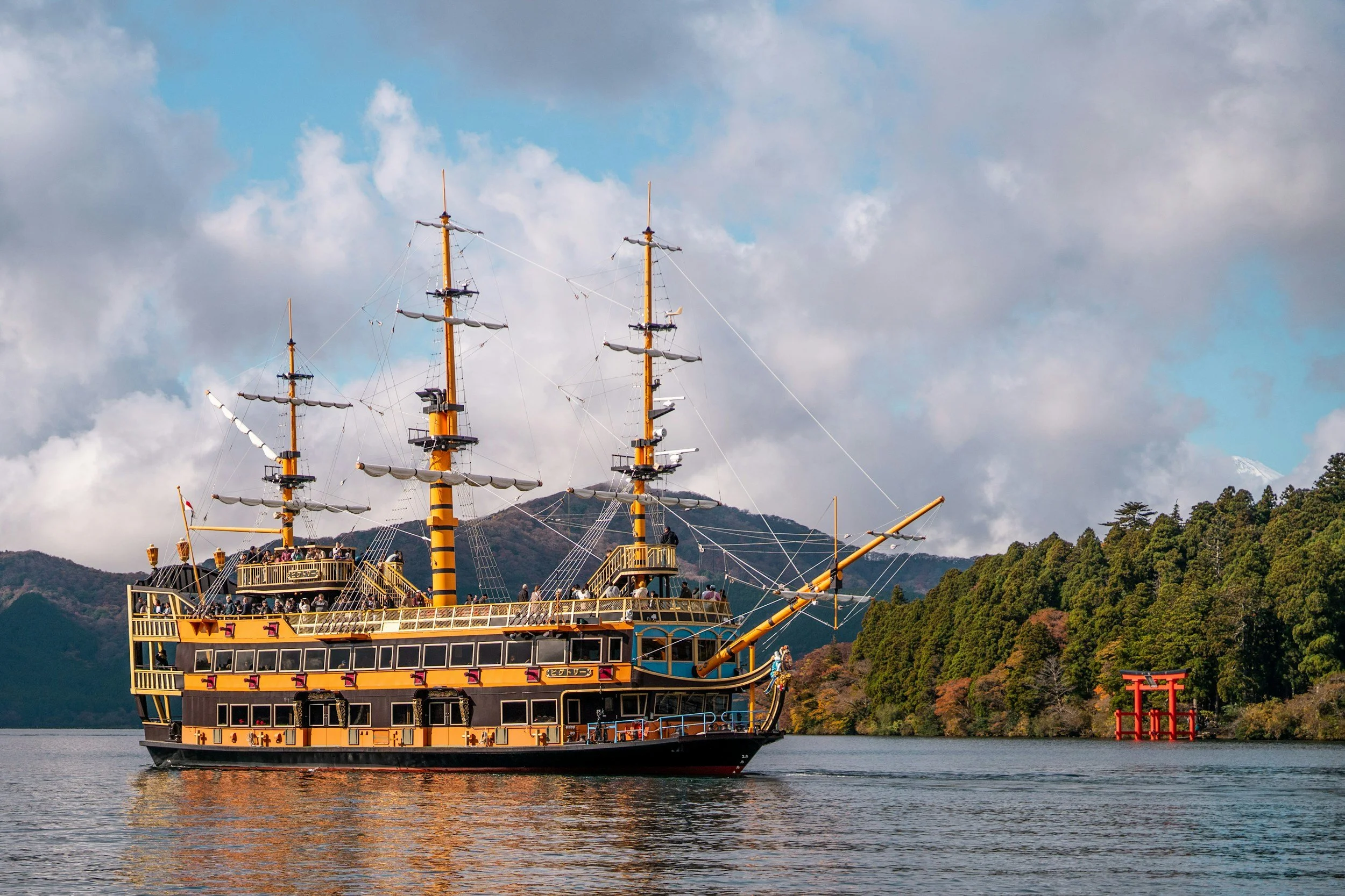 A large, colorful pirate ship-themed cruise boat sailing on a lake with lush, forested mountains in the background and a cloudy sky.