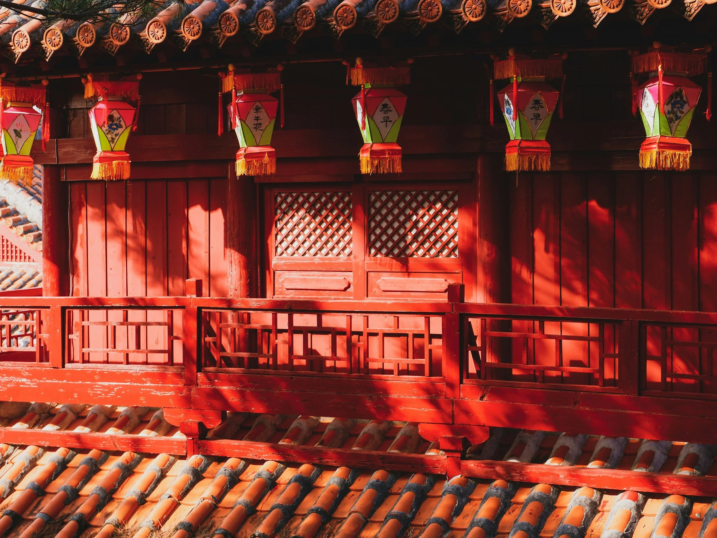 Red wooden and tiled roof structure with small colorful Japanese lanterns hanging beneath the eaves.