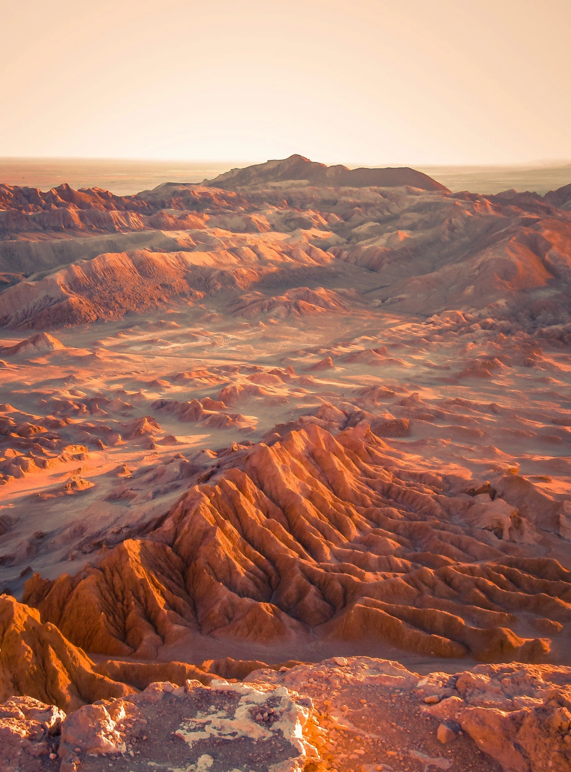 Sunset over a rugged desert landscape with reddish mountains and a distant horizon.