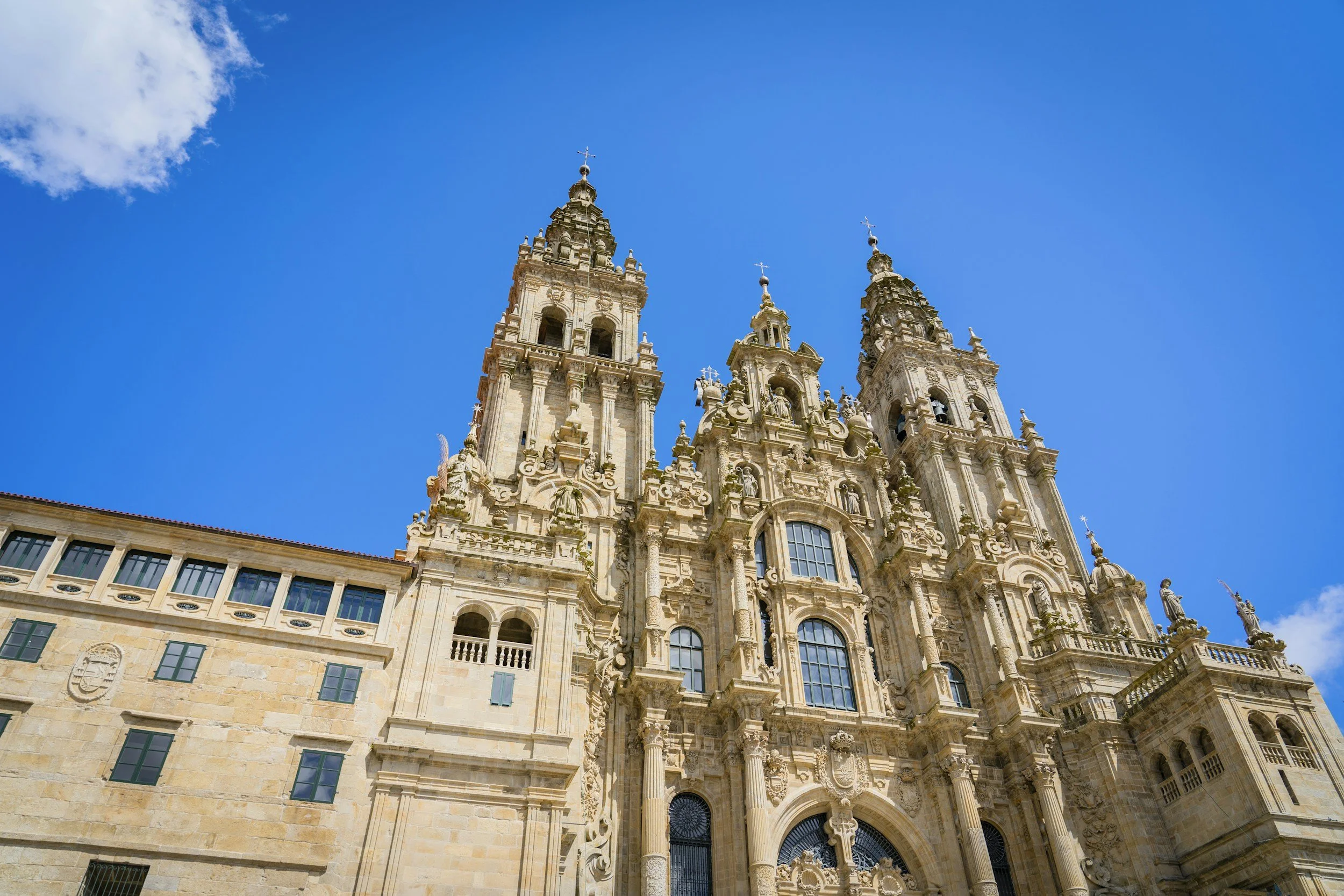 Facade of an ornate historic cathedral with two tall bell towers topped with crosses, set against a bright blue sky with a few clouds.