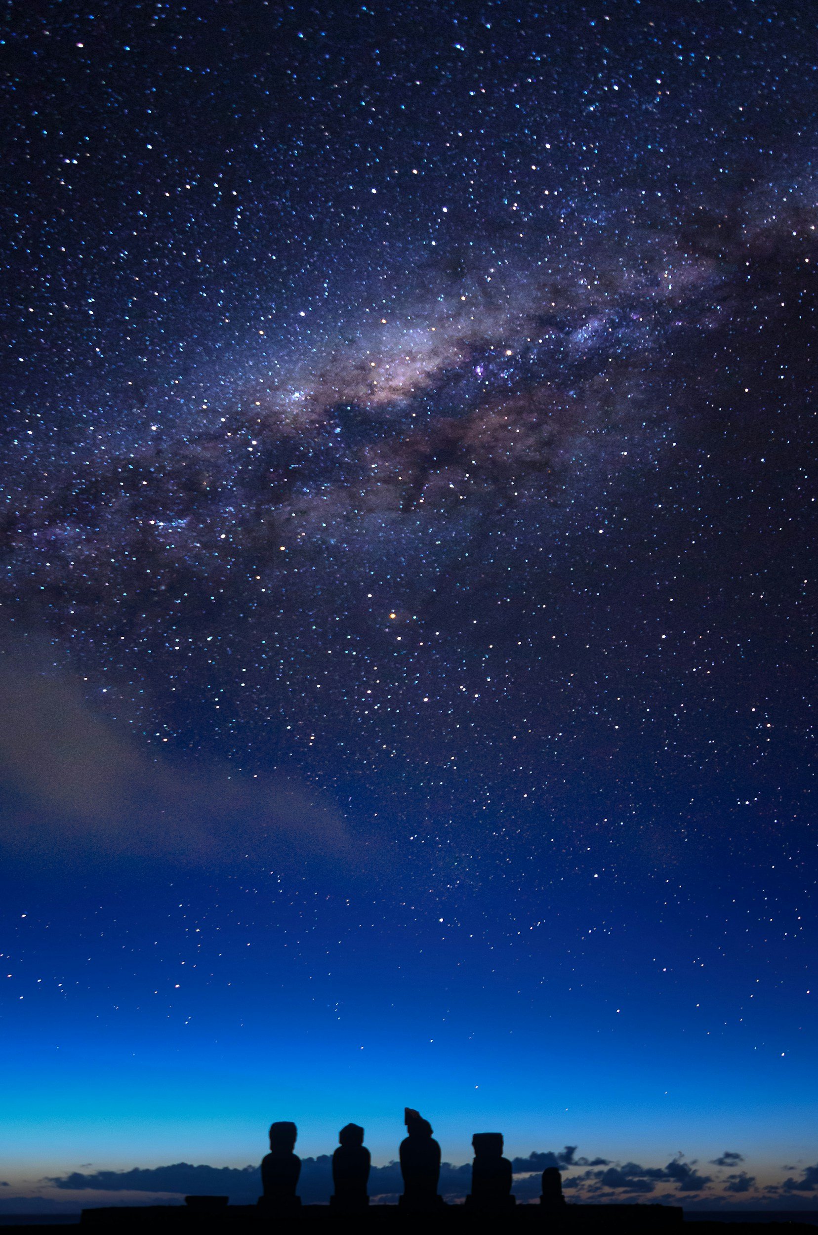Three silhouetted figures sitting on a stone structure, watching a starry night sky with the Milky Way galaxy visible above.