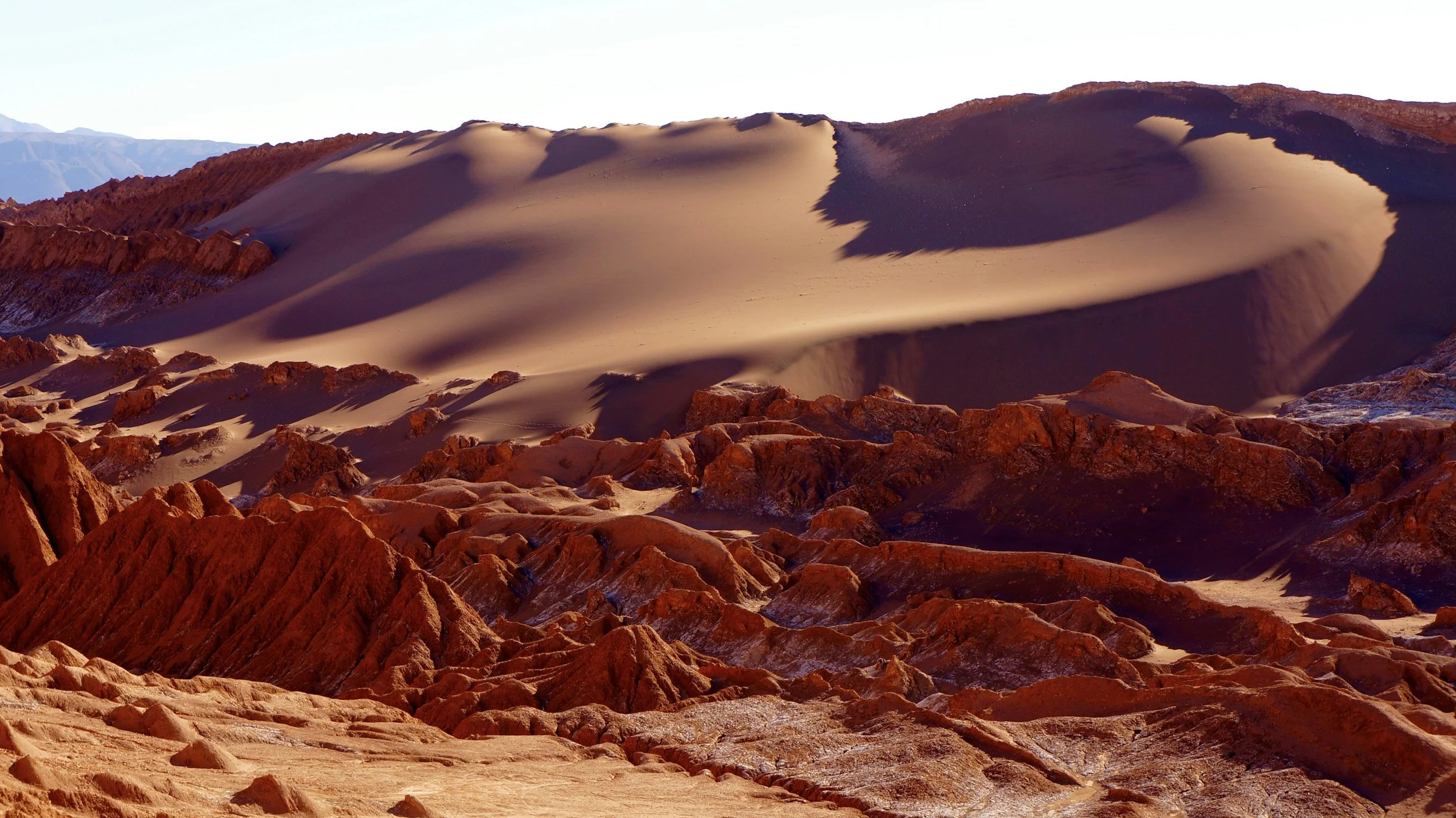 Red rock formations and sand dunes stretching toward the Andes in Chile's Atacama Desert