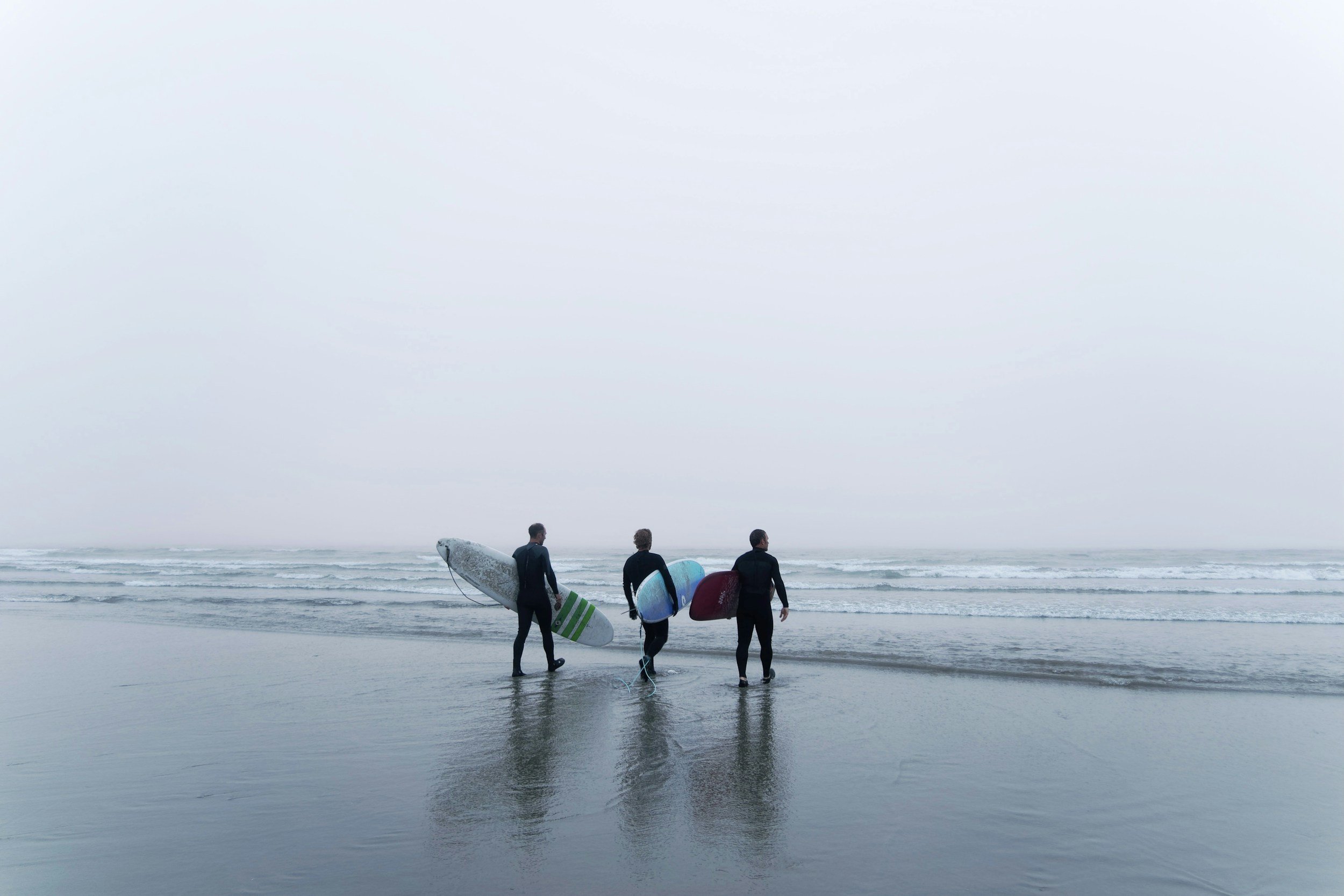 Surfers carrying boards through the mist along a Pacific beach in Tofino, British Columbia