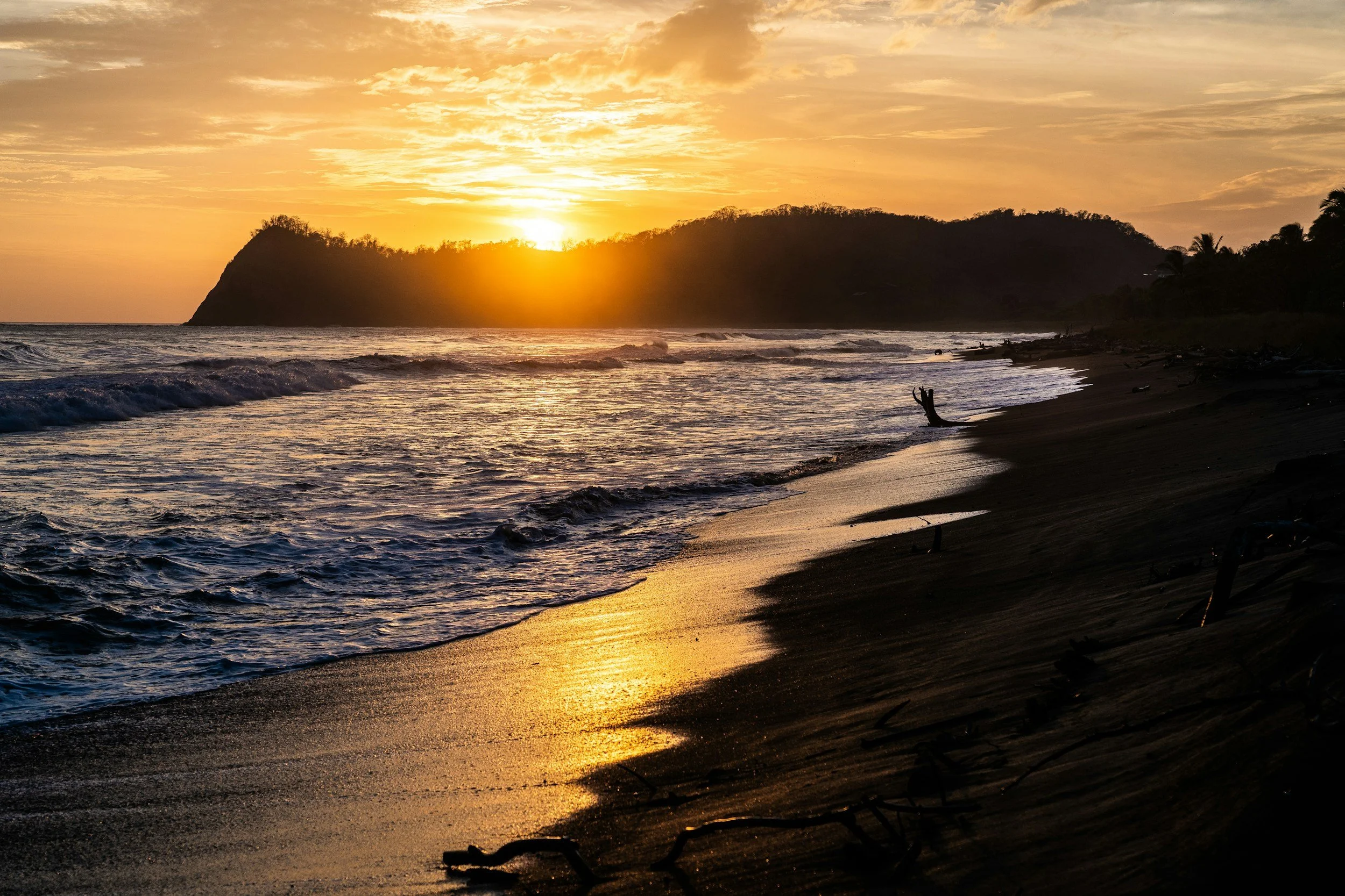 Golden sunset glowing behind a forested headland as waves roll onto a beach in Guanacaste, Costa Rica