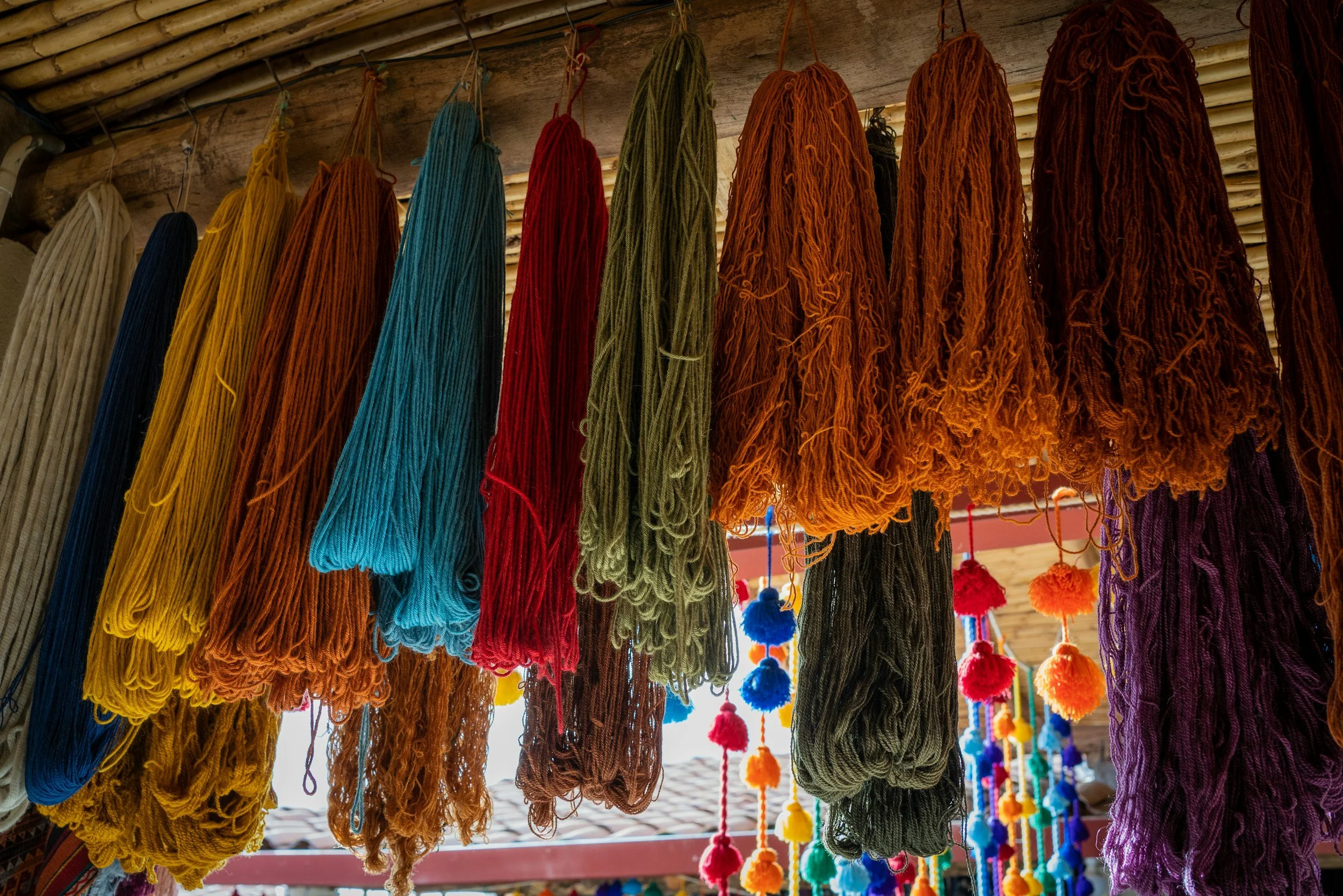 Bundles of naturally dyed alpaca yarn in rich reds, golds, greens, and blues hanging at a weaving cooperative in Chinchero.