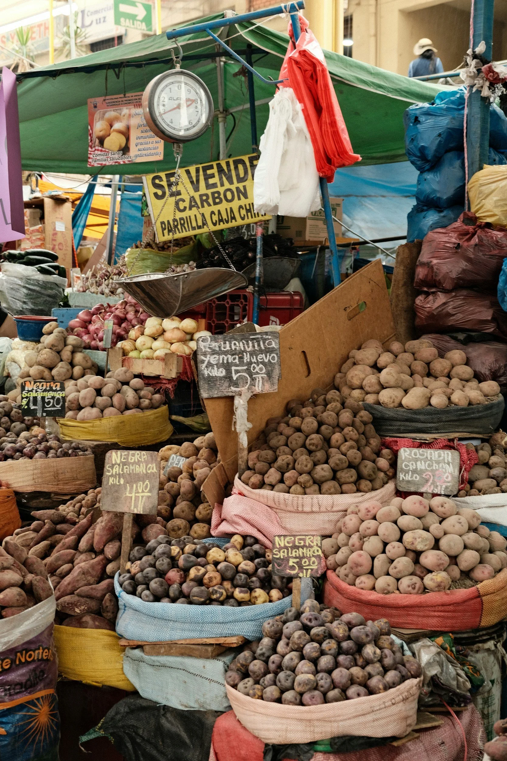 Heaps of colorful native Peruvian potatoes for sale at a highland market, with handwritten price signs.