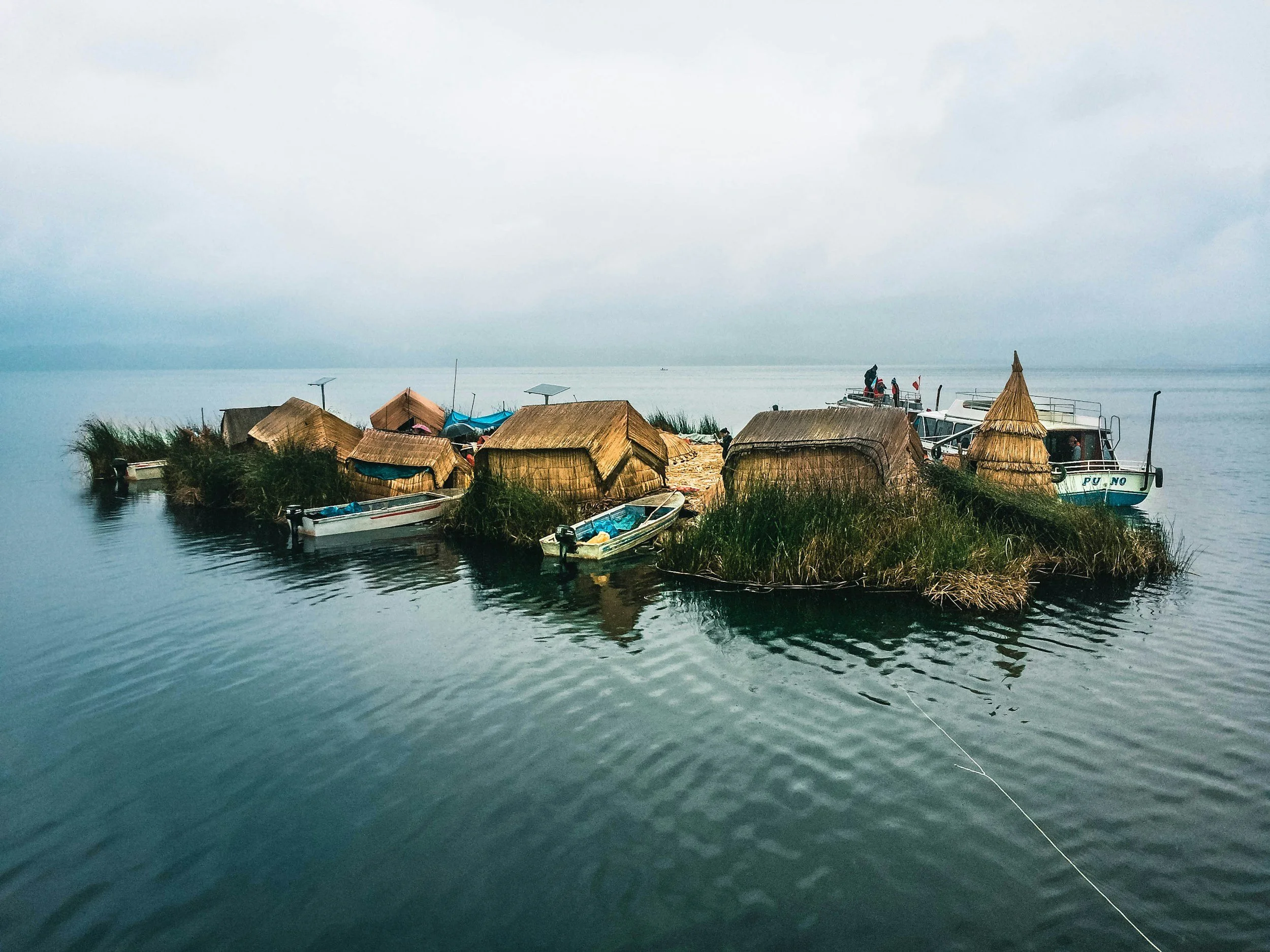 Thatched reed huts and small boats on a floating Uros island in the calm waters of Lake Titicaca.