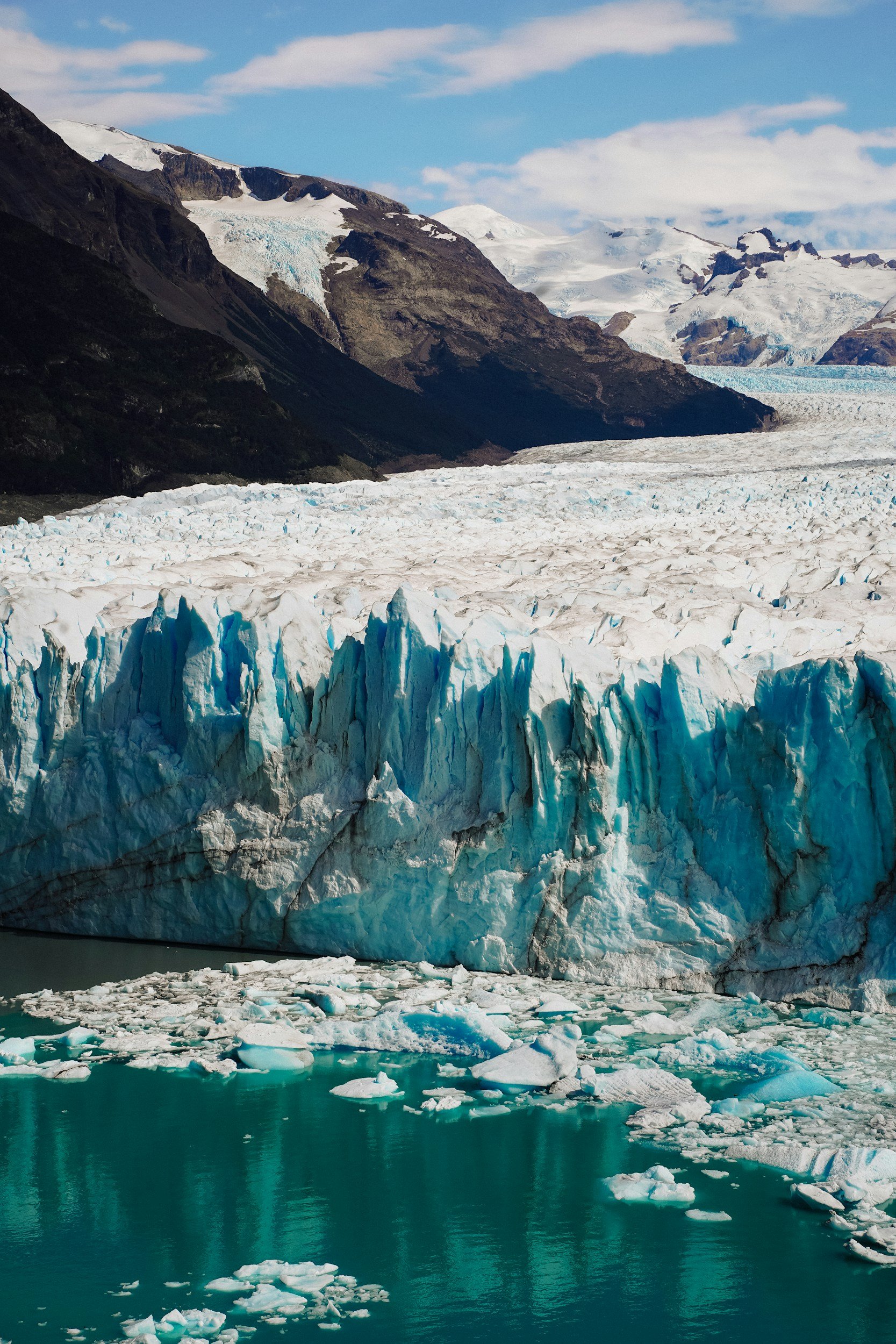 Jagged blue ice of Perito Moreno Glacier rising above floating ice in turquoise water.