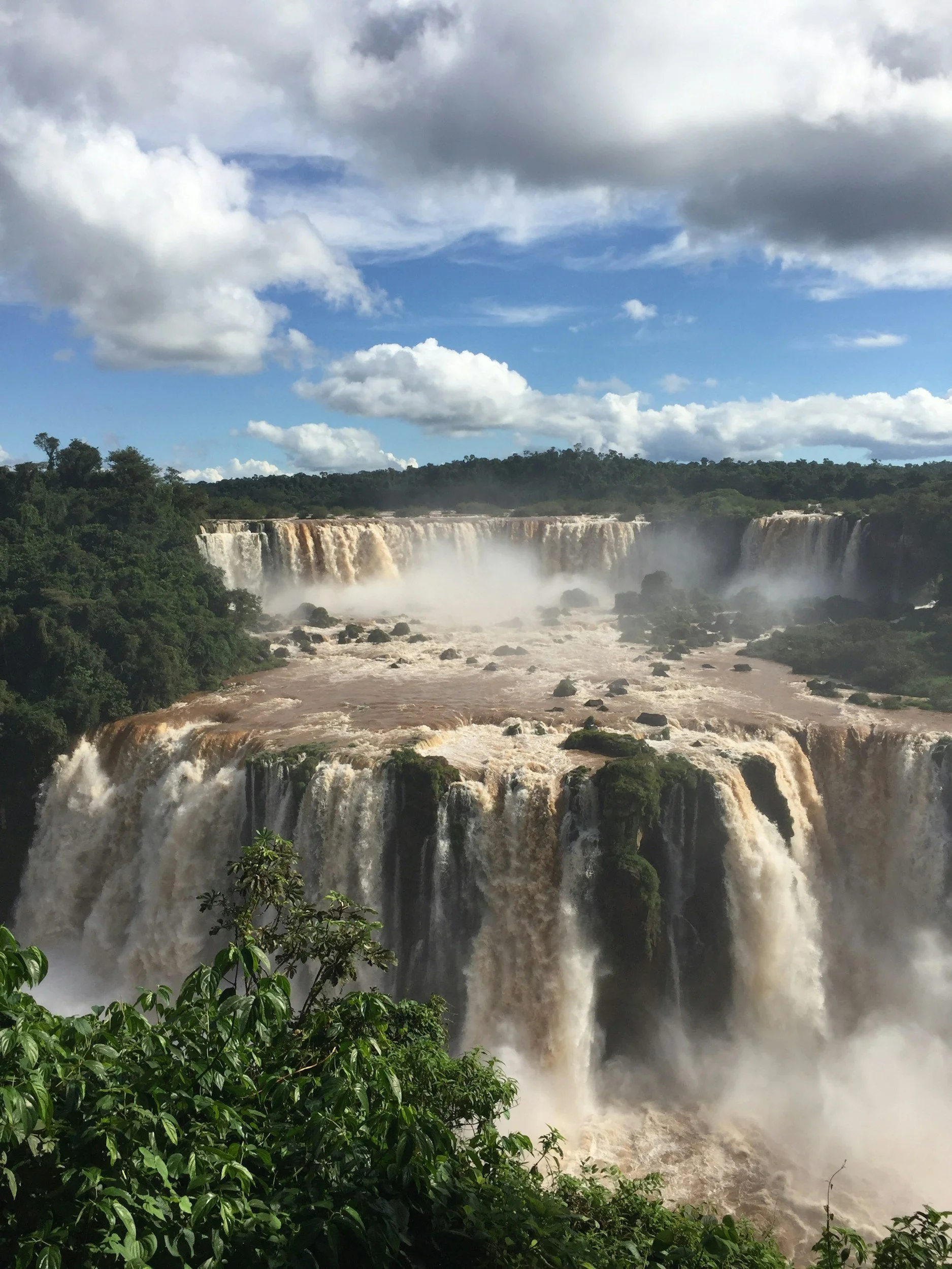 Powerful waterfalls pouring over rocky cliffs into mist surrounded by rainforest at Iguazú.