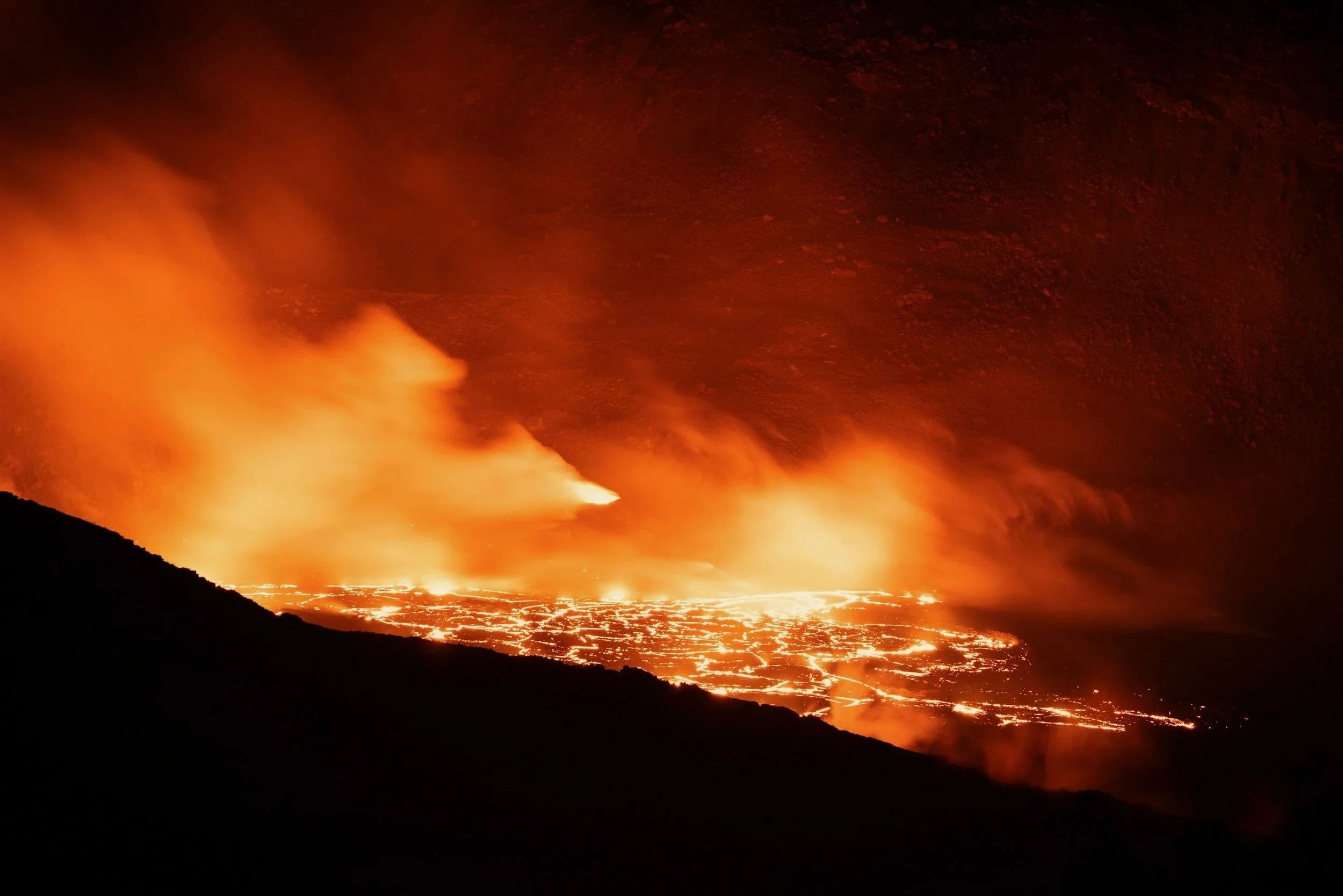 Glowing orange lava and steam rising from an erupting volcano at night on Hawai'i's Big Island