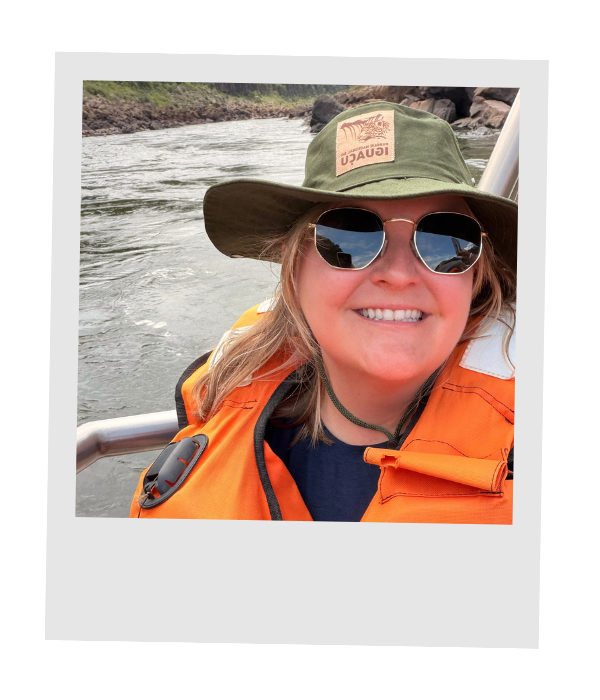 Piper smiling in a sun hat, sunglasses, and an orange life jacket on a river boat ride.