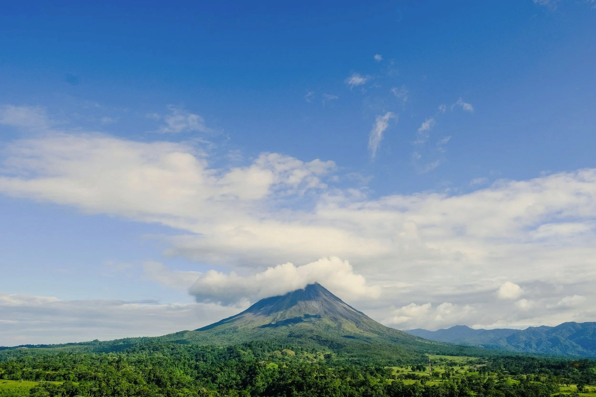 Arenal Volcano rising above the green rainforest on a sunny day with scattered clouds, Costa Rica