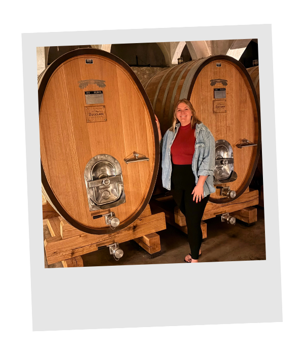 Piper standing between large oak wine vats in a Mendoza winery cellar.