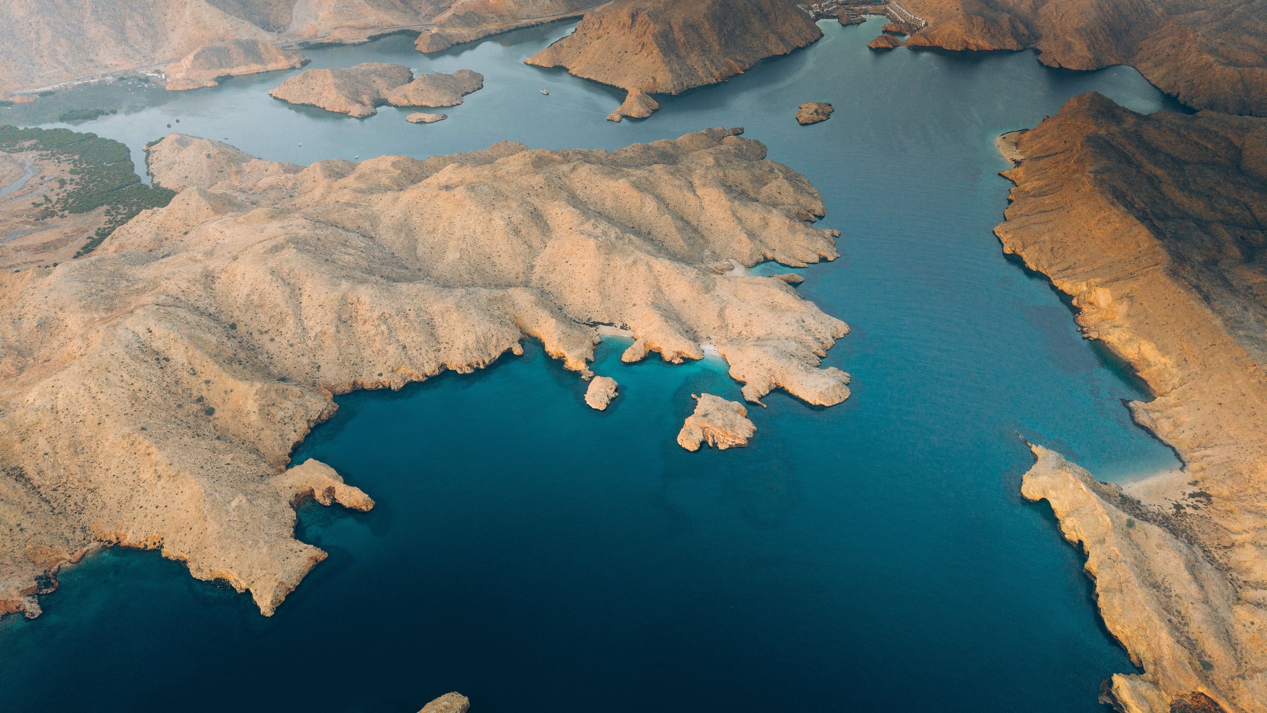 Aerial view of a large reservoir with a series of small islands and rugged, arid hills surrounding the water.