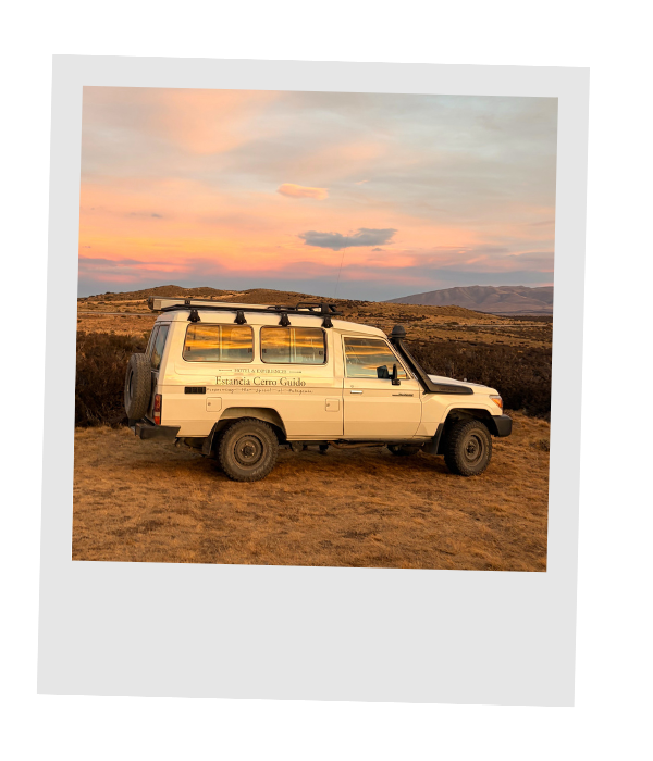 A white 4x4 expedition vehicle parked on the Patagonian plains beneath a pink and orange sunset.