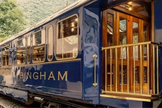 A navy blue Belmond Hiram Bingham train car with polished wood doors and a brass-railed open-air platform.