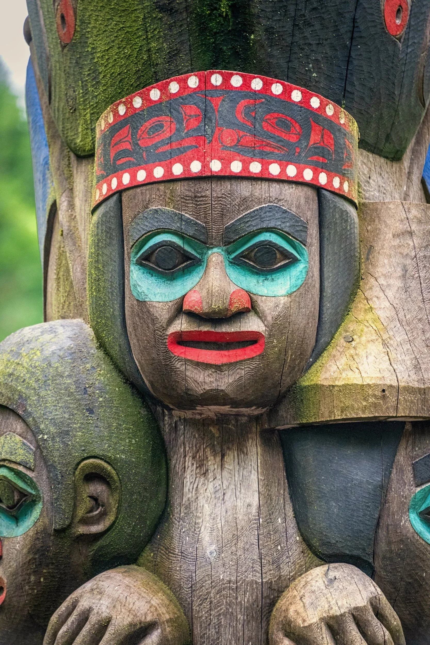 Carved and painted totem pole face with turquoise and red details in Alaska