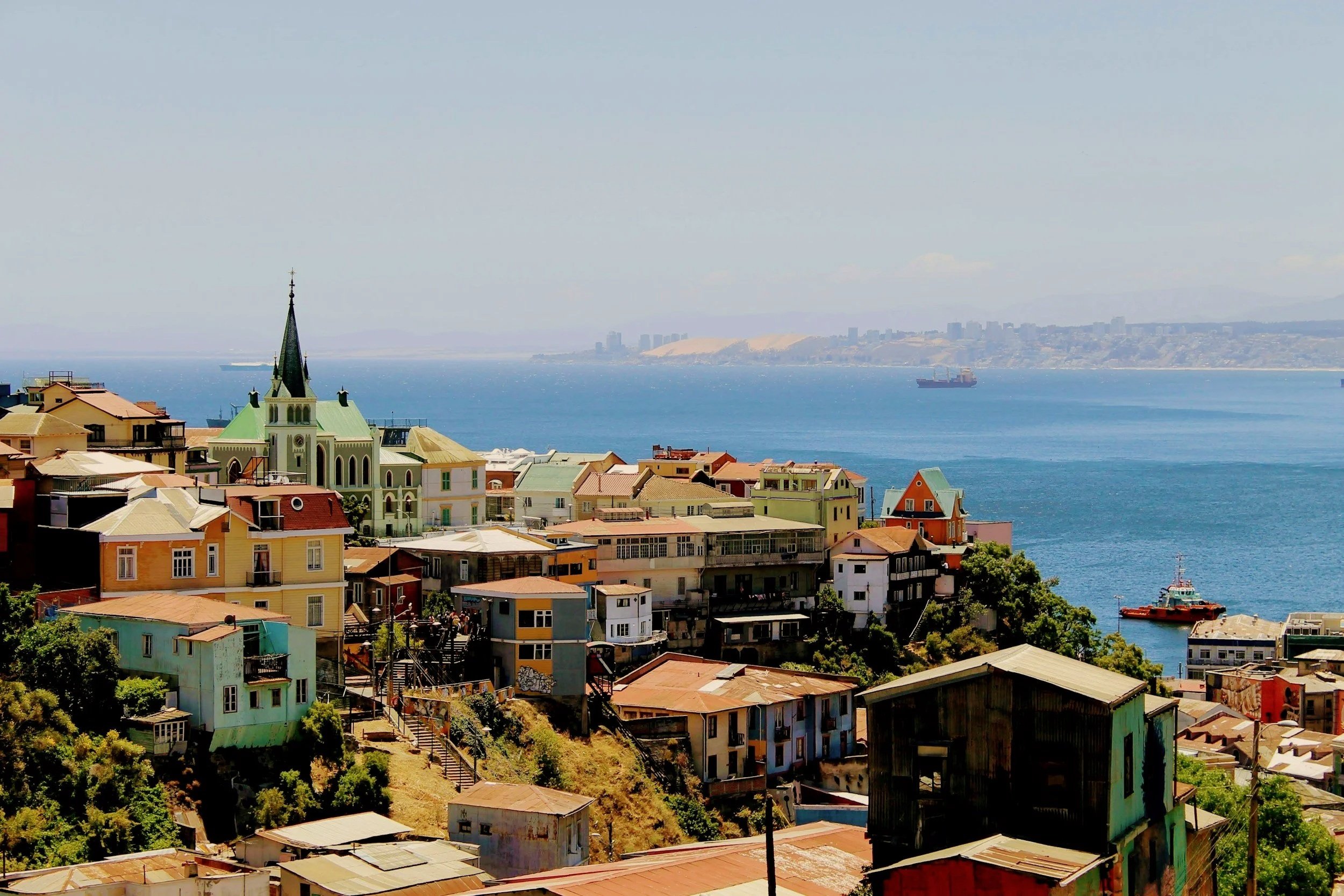 Colorful houses and a church spire climbing the hillsides of Valparaíso above a blue bay.