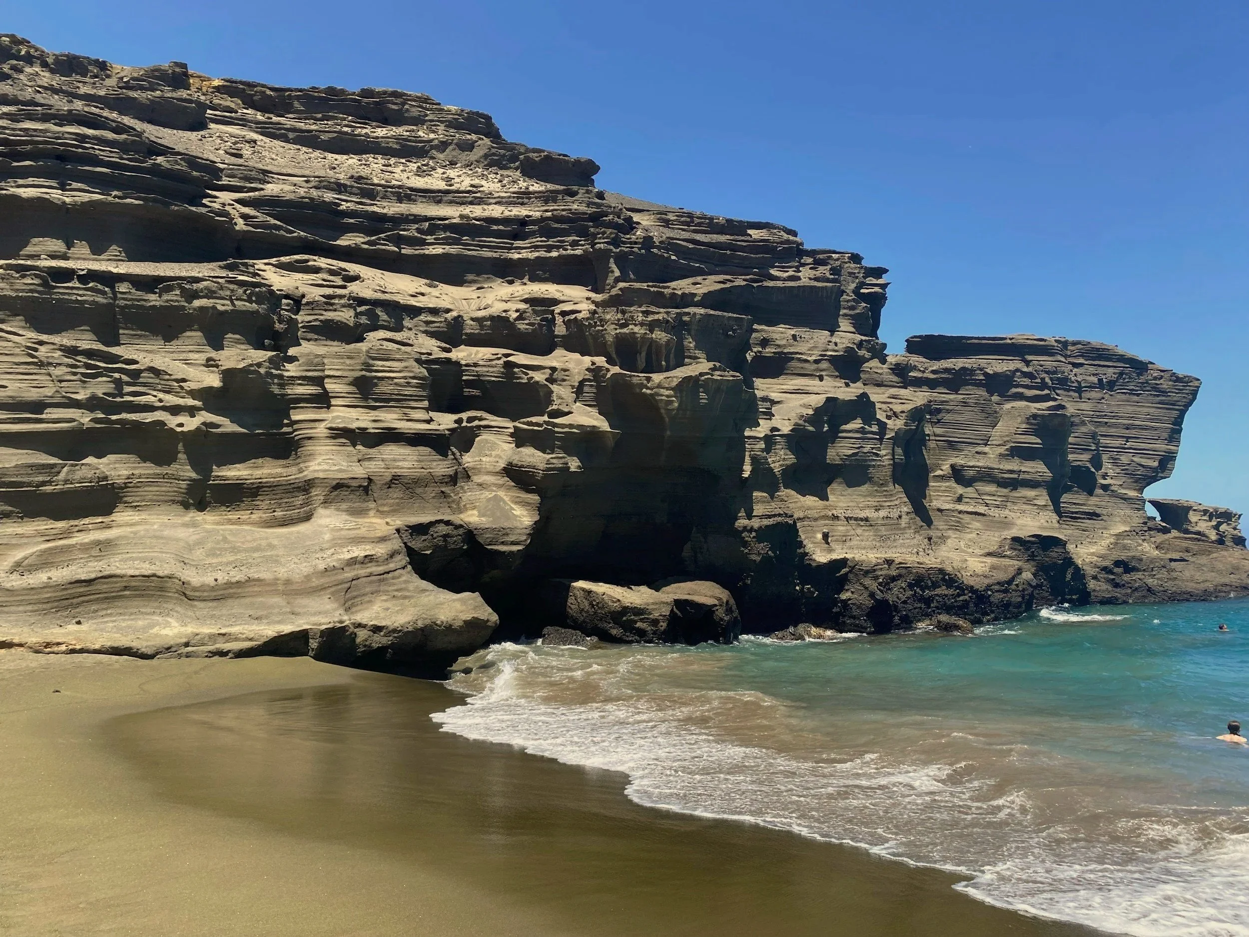Olive-green sand and ancient cinder cone cliffs at Papakōlea Beach on Hawai'i's Big Island