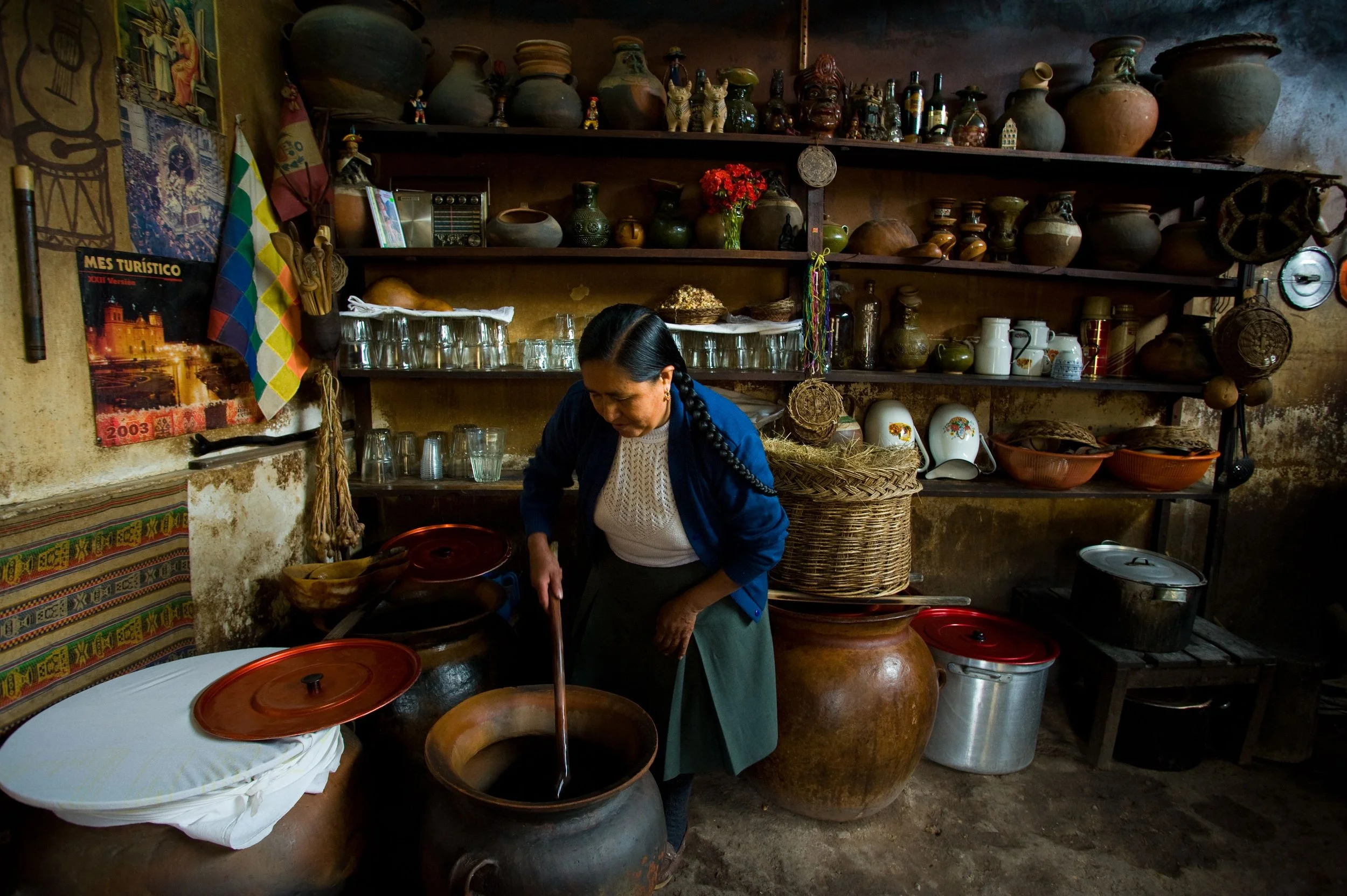 A woman in a traditional kitchen stirs a pot, surrounded by rustic cookware and decor.