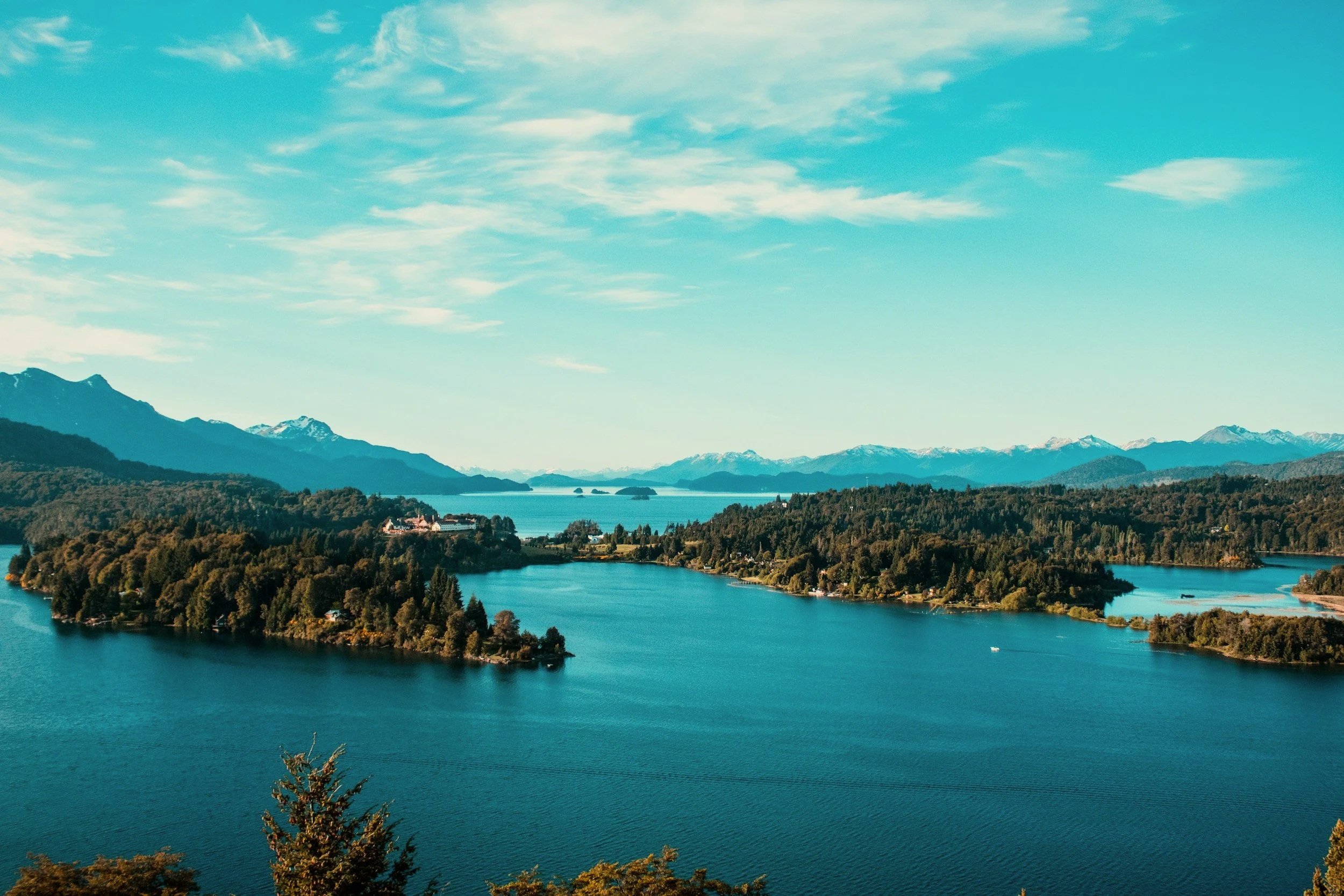 A deep blue lake curving around forested peninsulas with mountains on the horizon in Argentina's Lake District.