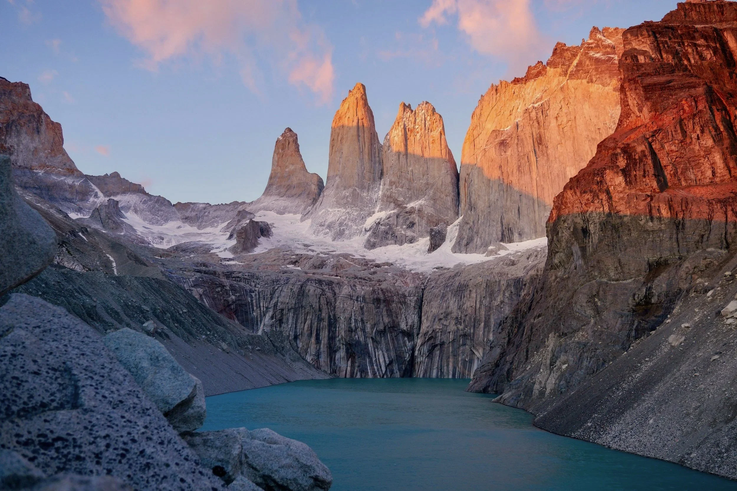 The three granite towers of Torres del Paine glowing orange at sunrise above a glacial lake.