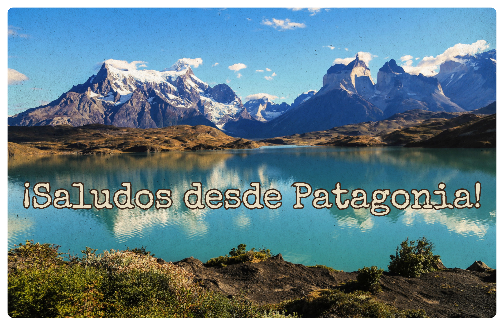 Snowcapped granite peaks of Torres del Paine reflected in a turquoise glacial lake, with the words ¡Saludos desde Patagonia!