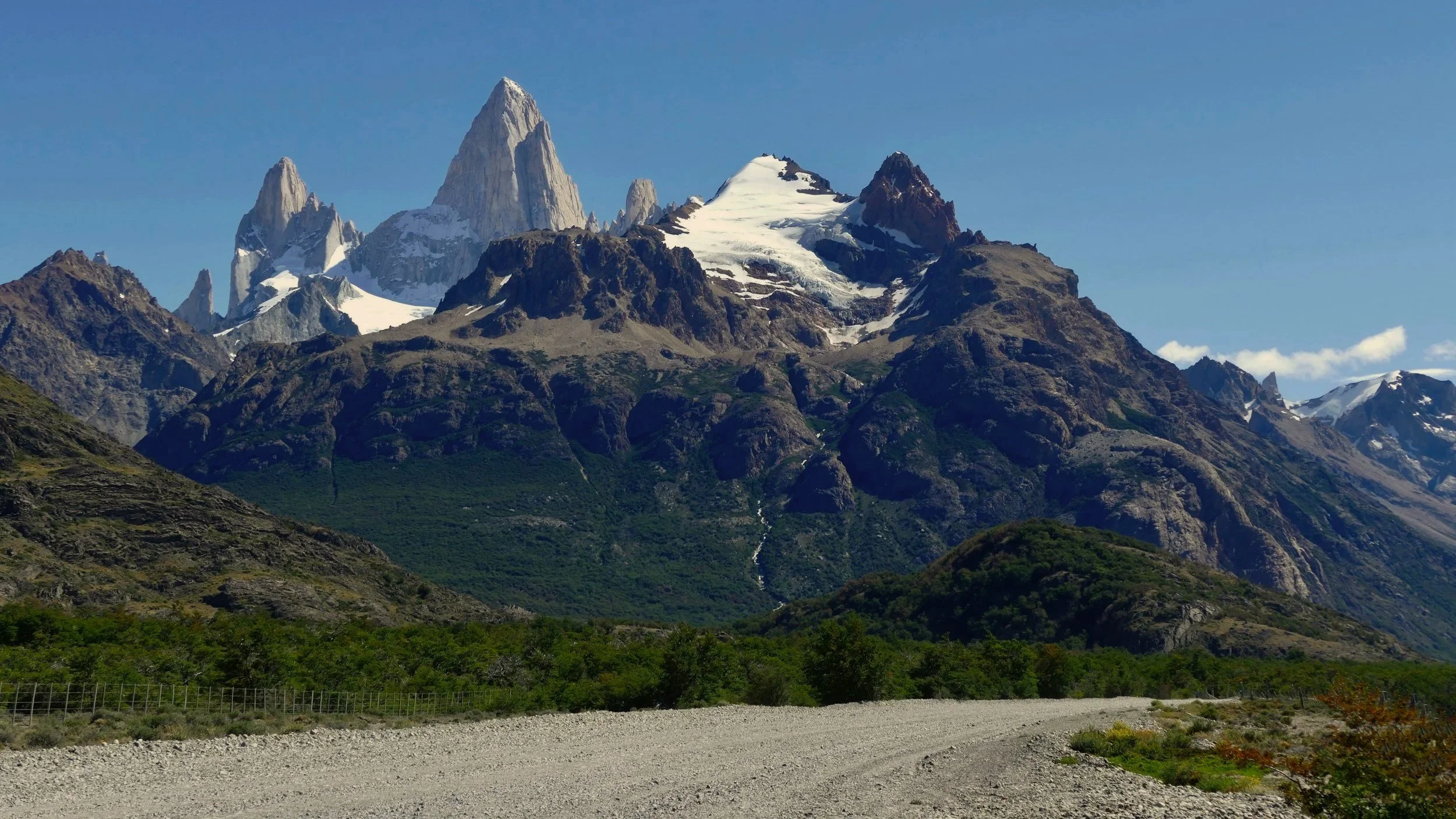The granite spires of Mount Fitz Roy rising above forested slopes and a gravel road.