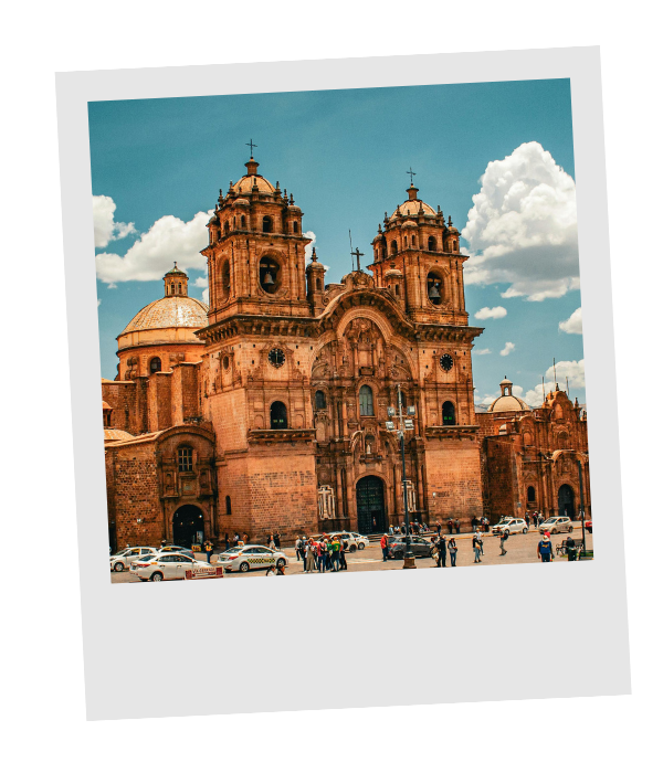 A historic stone church with twin bell towers under a partly cloudy sky, with people and cars in front.
