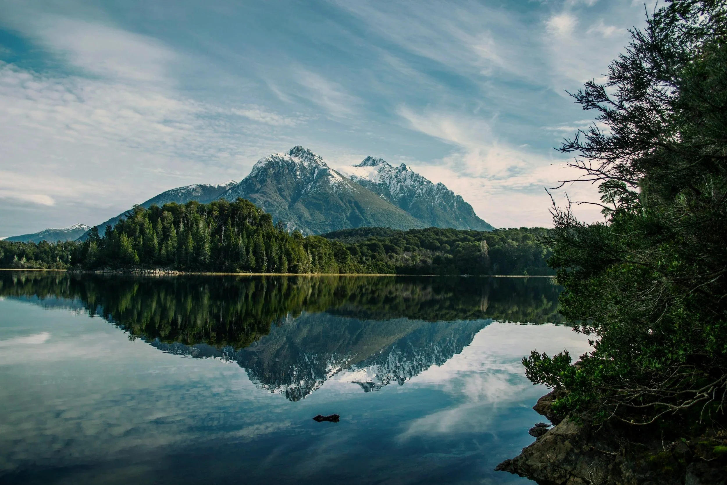 A forested mountain and snowy peak mirrored in a still alpine lake near Bariloche.