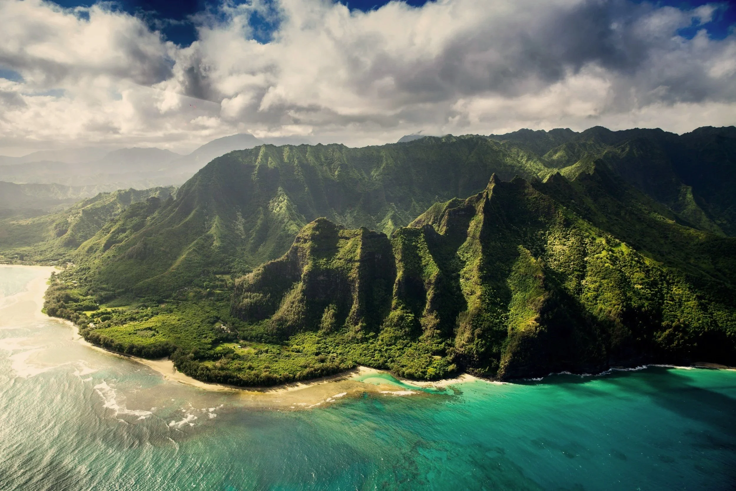 Green fluted cliffs of the Nāpali Coast rising above a turquoise bay on Kaua'i, Hawai'i