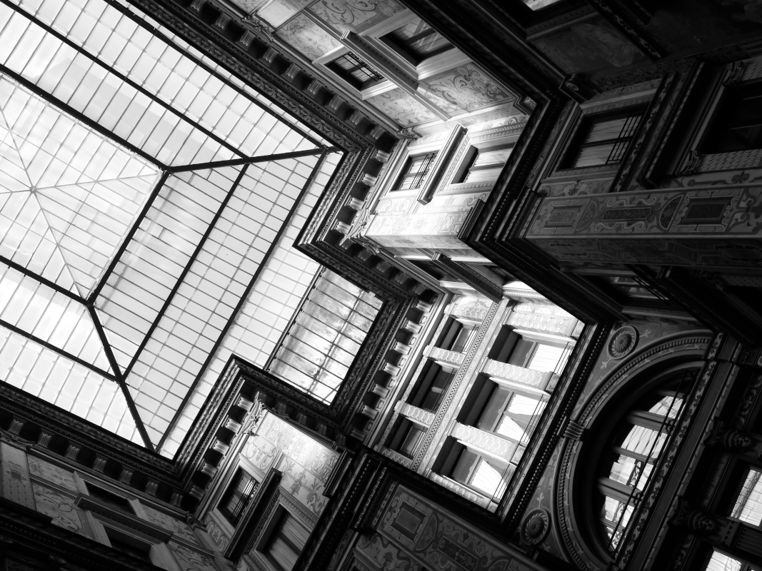 Looking up at a glass-domed ceiling inside a building with ornate architectural details in black and white.
