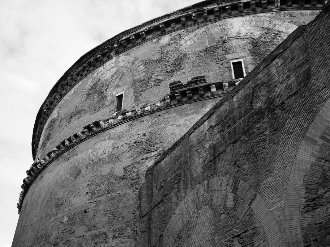 Black and white photo of the upper part of an old brick tower or building with small windows and decorative brickwork, viewed from below.