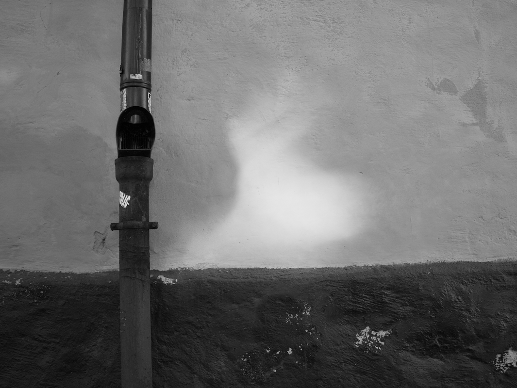 A downspout casting a shadow on a textured wall with peeling paint.