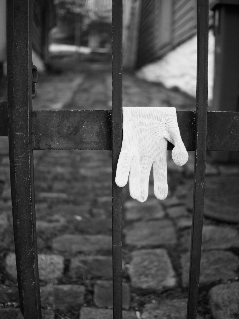 Close-up of a white glove hanging on black metal gate, stone pathway and blurred outdoor background.