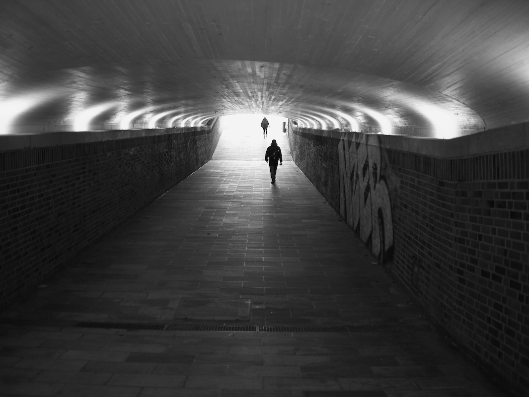 Two people walking through a tunnel with graffiti, illuminated from the exit at the far end.
