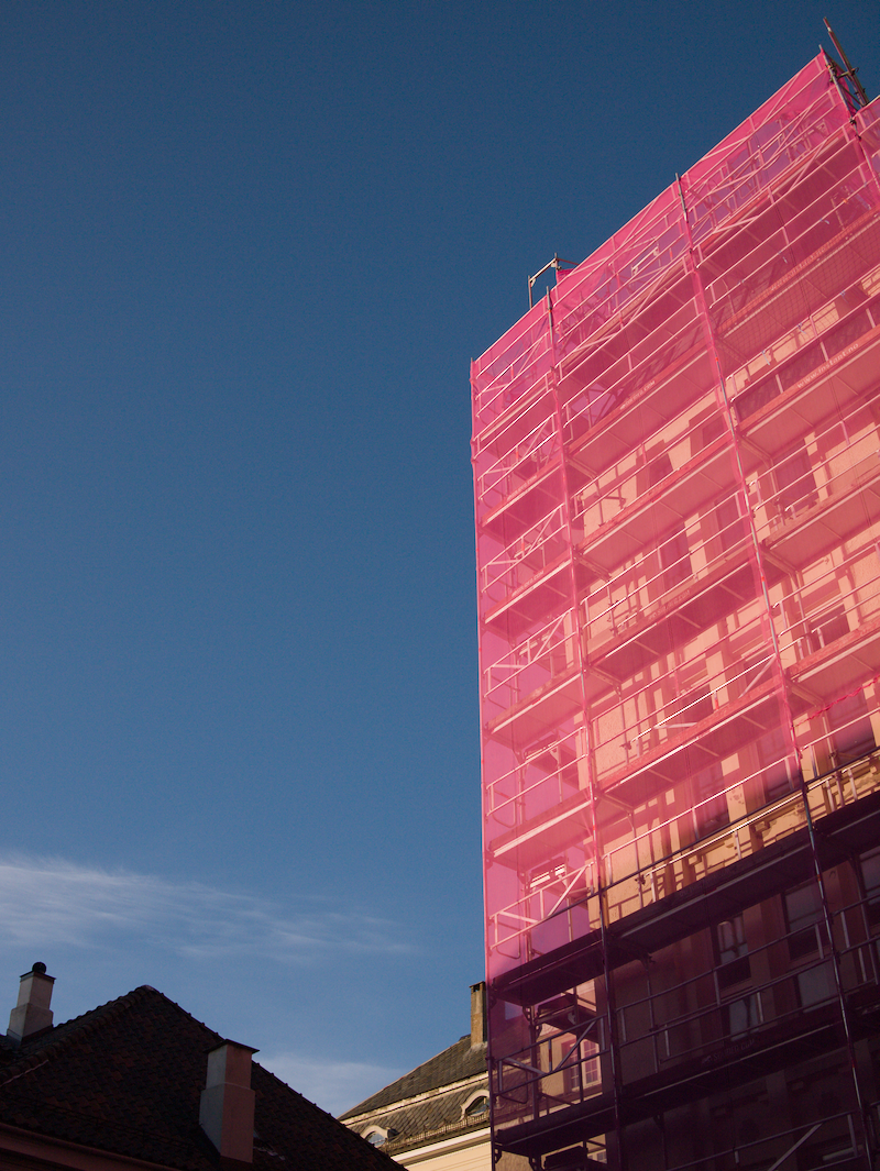 Close-up of a modern building with pink glass windows and balconies against a clear blue sky.