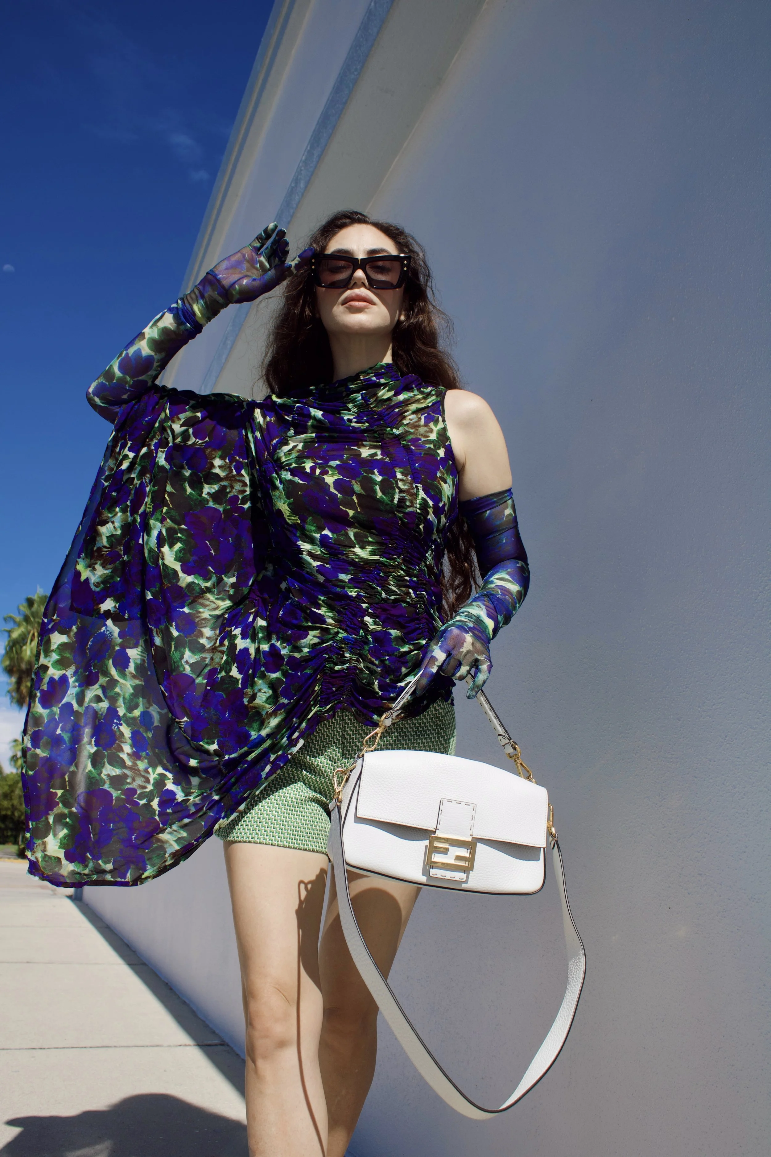 a model walks toward the camera wearing a dries van noten top and gloves, a fendi baguette bag, and green shorts