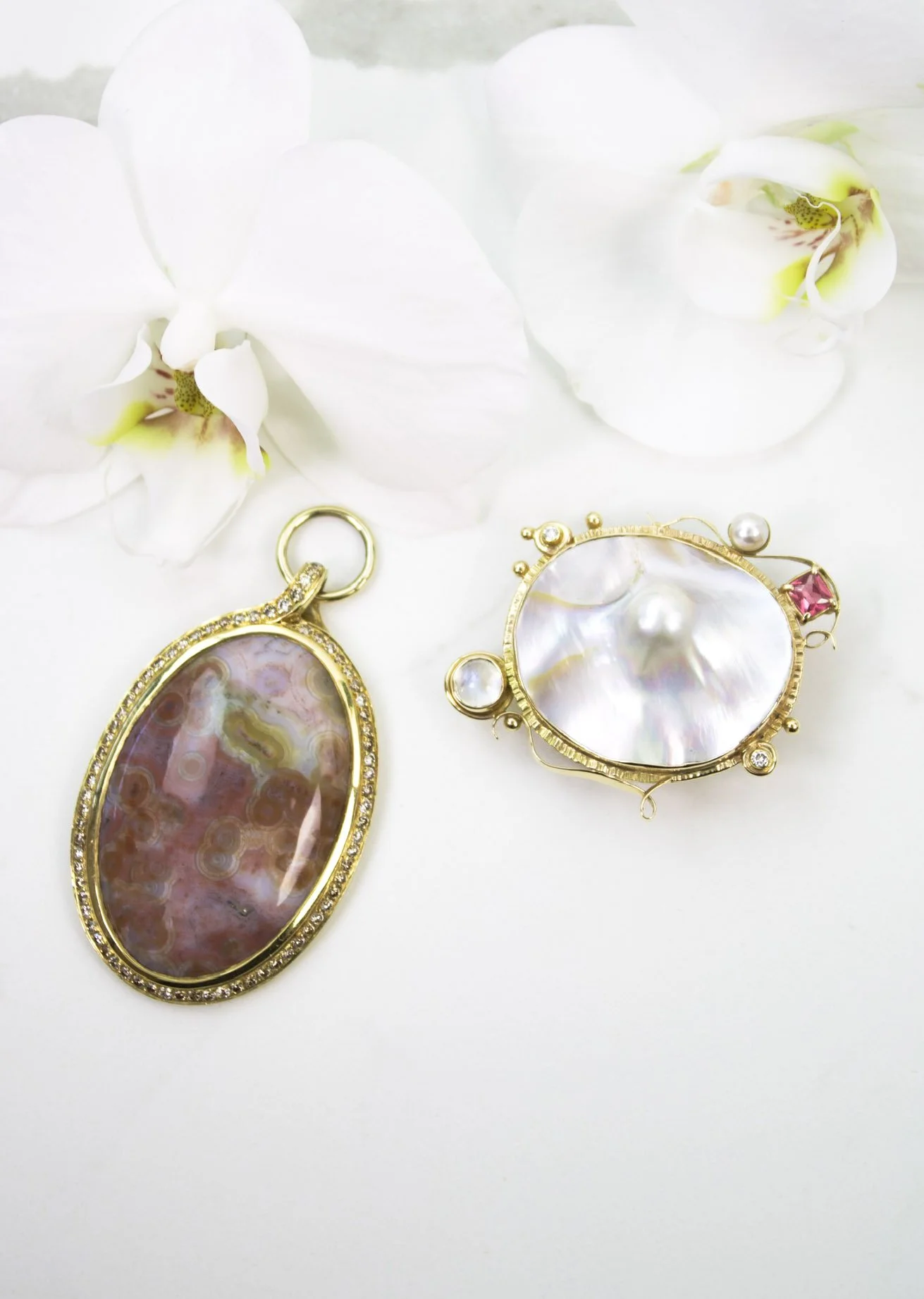 product shoot of two gold and rare gemstone pins on a marble table with orchids